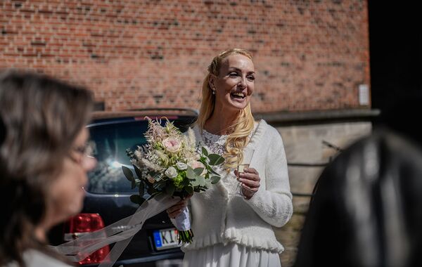 Braut hält Brautstrauß und Sektglas und lacht.