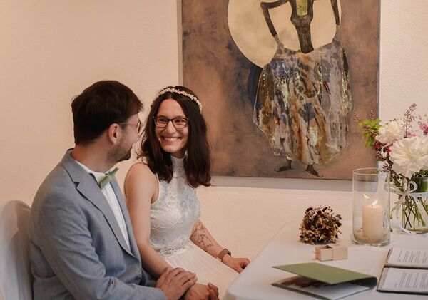 Brautpaar sitzen im Trauzimmer und lächeln sich an.
