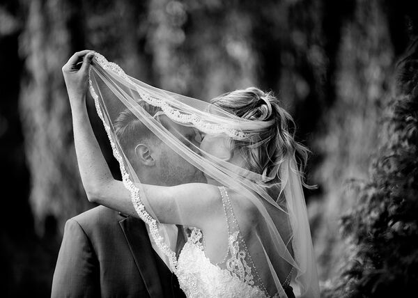 Braut hält ihren Schleier während sie sich küssen vor ihren Gesichtern.