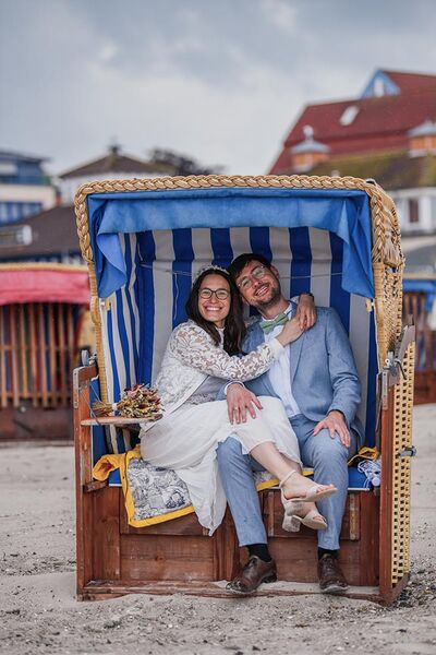 Brautpaar sitzt im Strandkorb und lächelt in die Kamera.