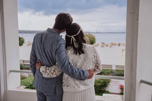 Brautpaar steht auf Balkon und schaut auf den Strand in Laboe und auf's Meer hinaus.