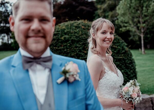 Im Vordergrund der Bräutigam unscharf. Die Schärfe liegt auf der Braut im Hintergrund.