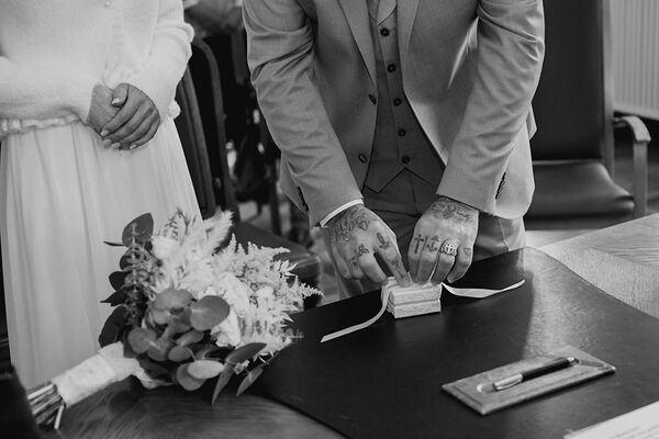 Bräutigam löst eine Schleife auf einer Ringschatulle. Bildausschnitt zeigt nur die Hände. Aufgenommen im Kieler Standesamt.