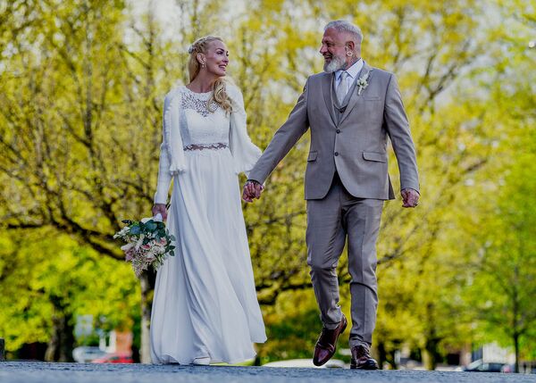 Brautpaar geht in Richtung Kamera, schauen sich an und lächeln dabei. Aufgenommen vor der Kieler Oper.