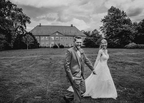 Brautpaar geht schnell auf einer Wiese und lächeln. Im Hintergrund ist das Gut Borghorst zusehen.