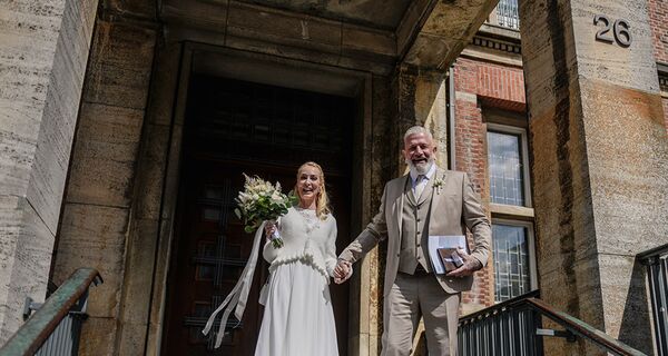 Brautpaar vor dem Kieler Standesamt- lachend in die Kamera.