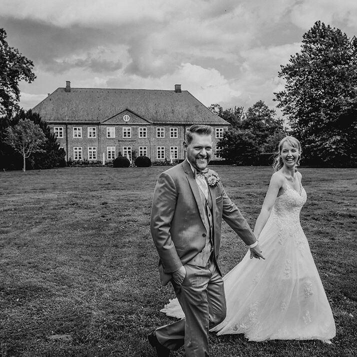 Brautpaar geht schnell auf einer Wiese und lächeln. Im Hintergrund ist das Gut Borghorst zusehen.