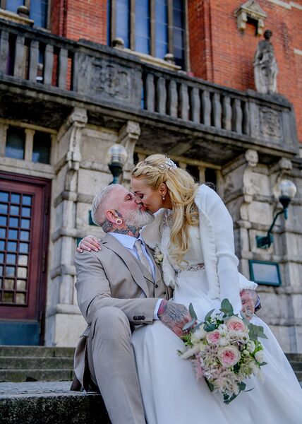 Brautpaar sitzt auf Treppenstufen vor der Kieler Oper. Die Braut sitzt dabei auf dem Schoß des Bräutigams. Sie küssen sich.