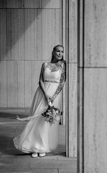Einzelaufnahme der Braut in Schwarz-Weiß. Sie lehnt sich an einer Säule an und schaut leicht lächelnd in die Ferne.