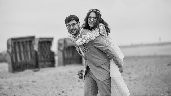 Hochzeitsfotografie Kiel - Bräutigam trägt Braut Huckepack am Strand
