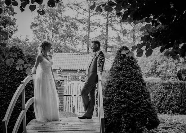 Brautpaar steht auf geschwungener weißer Brücke. Sie stehen sich gegenüber und lächeln sich an.